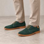 Men's dark green suede Derby shoes with tan laces worn in a neutral studio